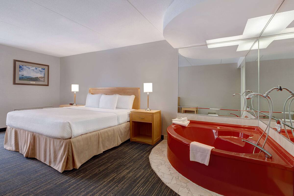 Une chambre d’hôtel avec un lit, des lampes de chevet, une baignoire rouge et un grand miroir.