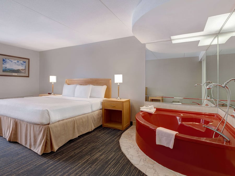 Quarto de hotel com cama, luminárias de cabeceira, uma banheira vermelha e um espelho grande.