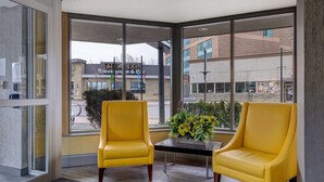 Un intérieur moderne avec deux fauteuils jaunes, une petite table et une grande fenêtre donnant sur un bâtiment avec une enseigne.