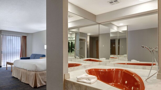 Une chambre d’hôtel avec un grand lit, un coin salon, une baignoire rouge et un grand miroir.