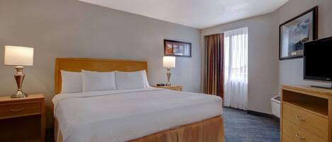 A hotel room with a large bed, two bedside tables with lamps, a television on a wooden cabinet, and a window with curtains.