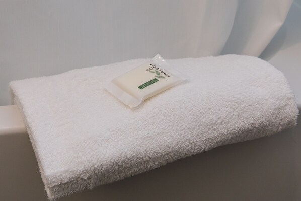 Une serviette blanche, soigneusement pliée, est posée sur une surface blanche. Un petit emballage portant l’inscription « Eco-Loc » se trouve sur le dessus.