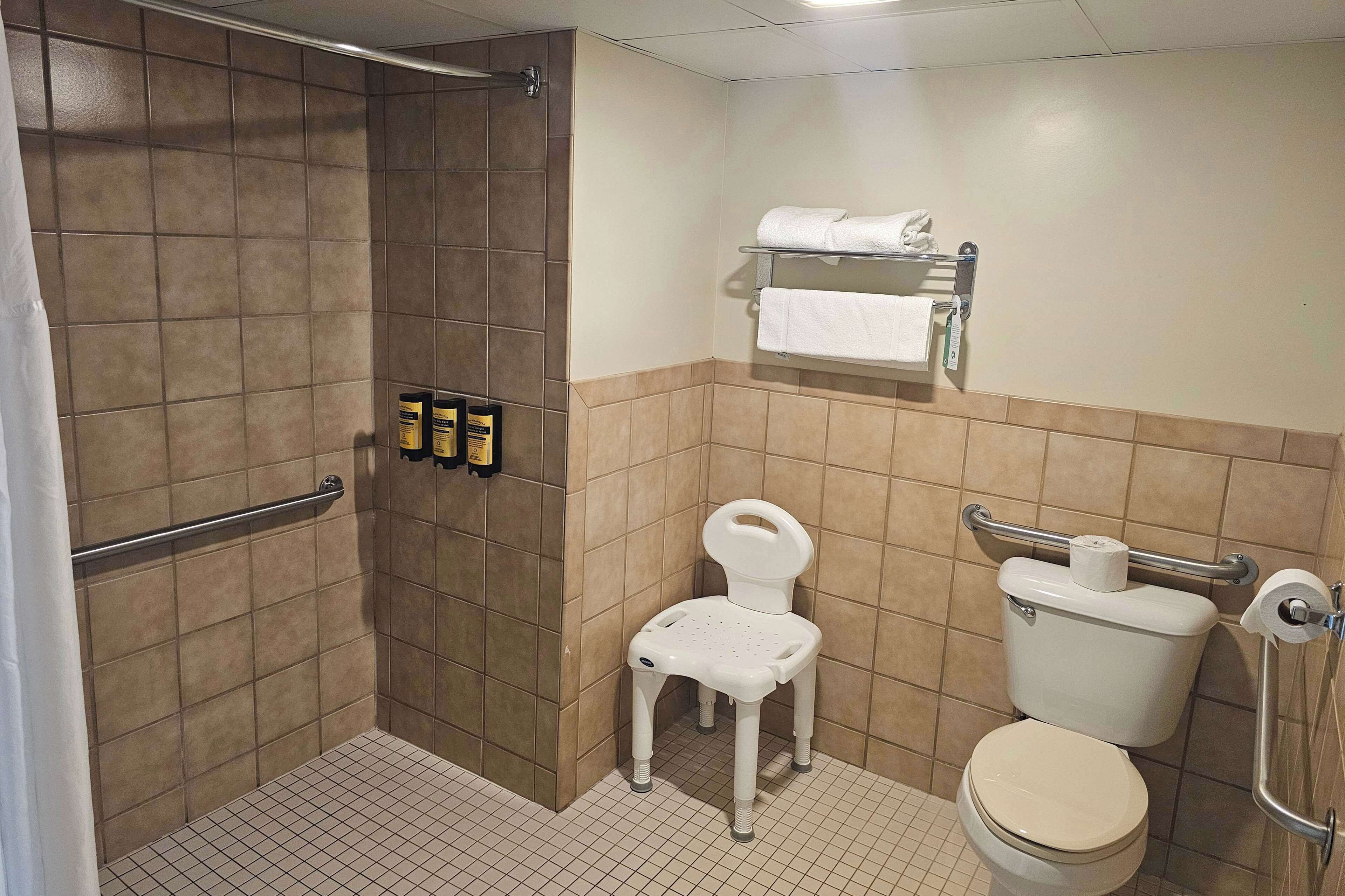 A small bathroom with a shower, a toilet, and a white plastic chair.