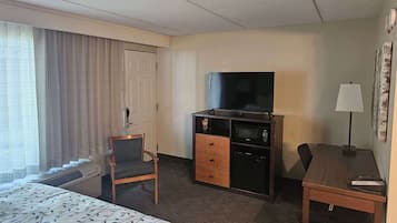 A hotel room with a bed, a desk, a chair, a TV, and a minibar.