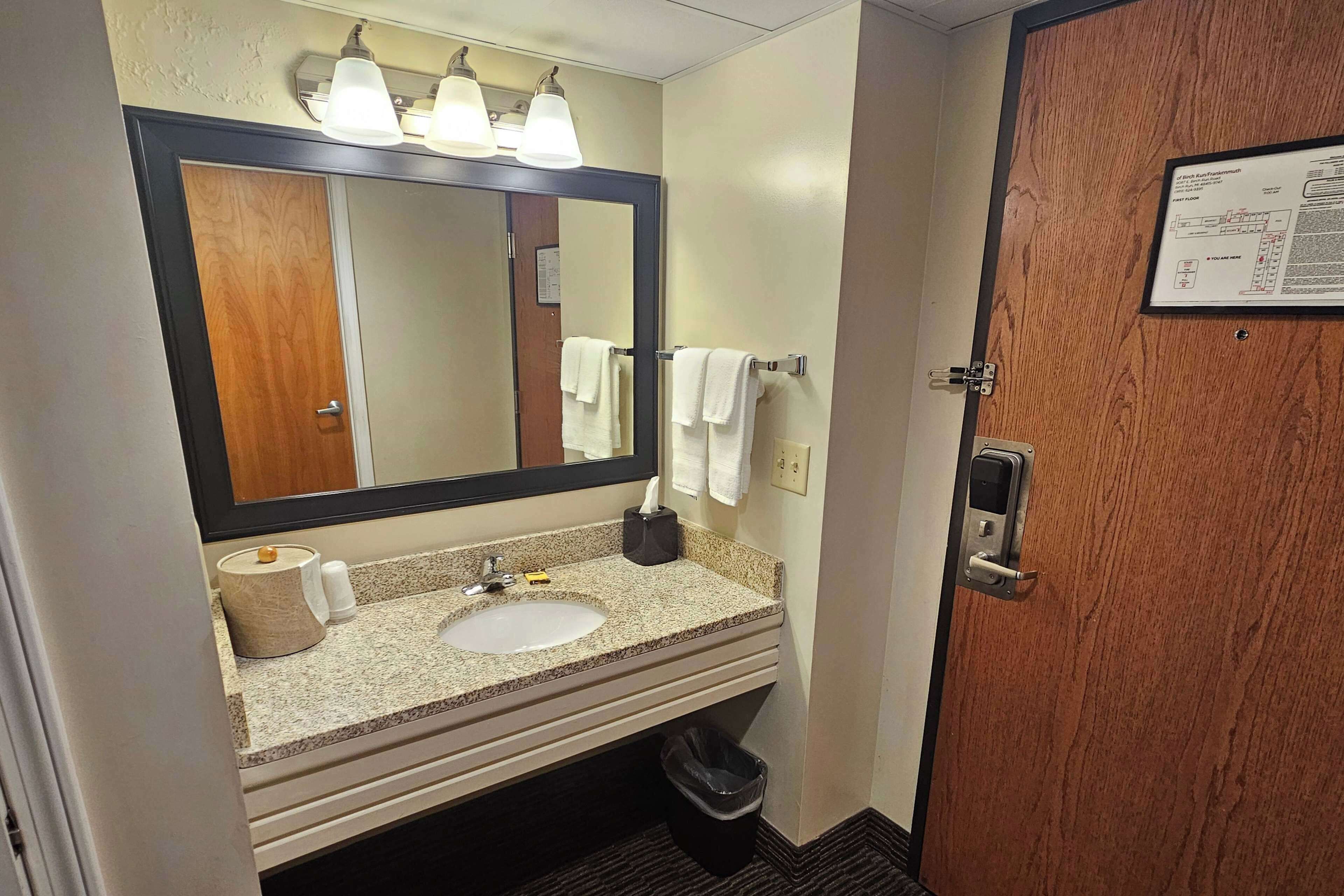 A hotel bathroom with a sink, mirror, towel rack, and a door with a lock.