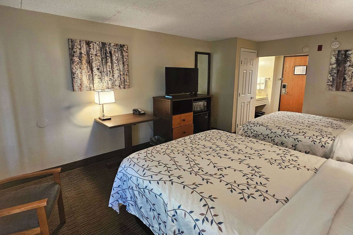 A hotel room with two beds, a desk with a lamp, a television, and a mirror.