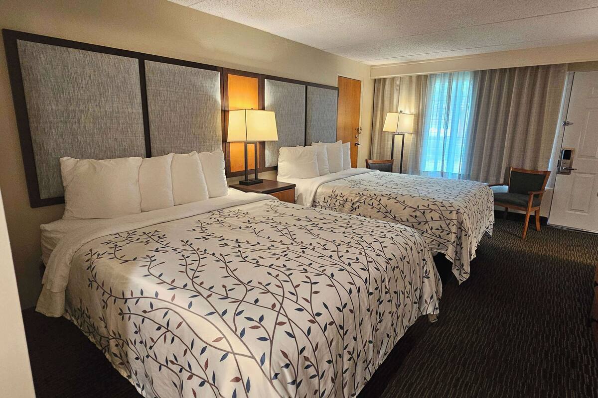A hotel room with two beds, a desk, and a chair.
