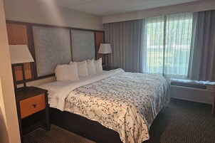 Quarto de hotel com uma cama grande, duas mesas de cabeceira com luminárias, uma janela com cortinas e um ar condicionado fixado na parede.