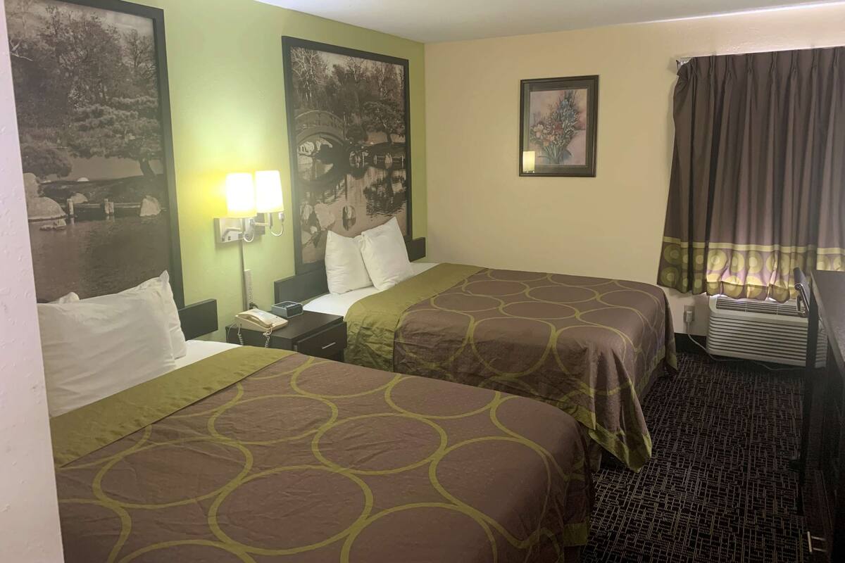 A hotel room with two beds, a nightstand with a phone, a lamp, and a painting on the wall.