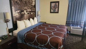 A hotel room with a bed, a nightstand, a lamp, a wall-mounted air conditioner, and a window with curtains. - Super 8 by Wyndham Galesburg (Galesburg)