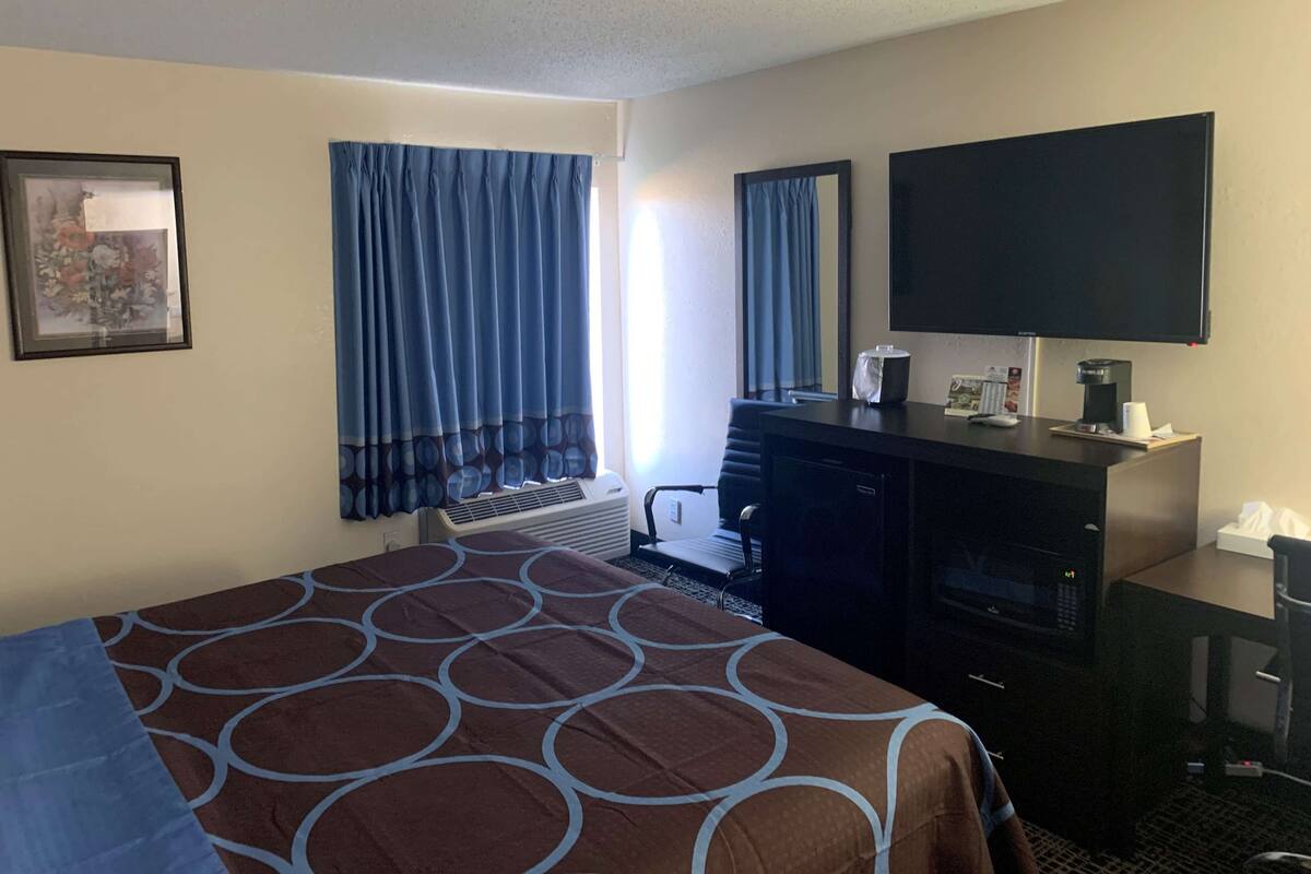 A hotel room with a bed, a desk with a flat-screen TV, a microwave, and a small seating area.