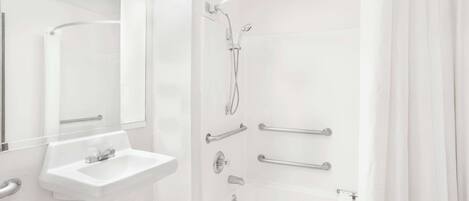 A modern bathroom with a white sink, a mirror, a shower with grab bars, and a bathtub.