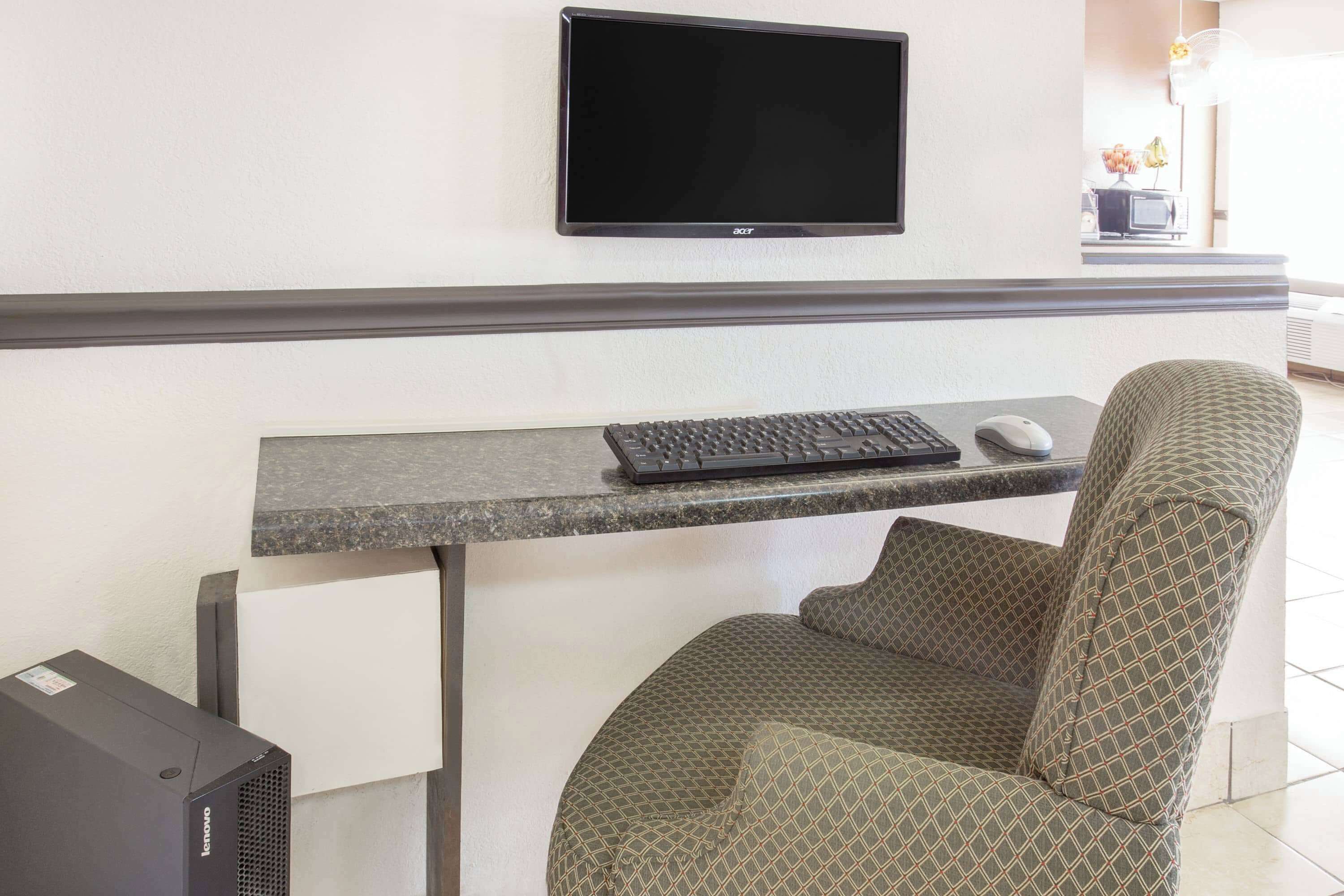 Un escritorio pequeño con teclado, ratón y monitor Acer. Hay una silla estampada y un ordenador de sobremesa Lenovo.