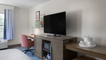 A hotel room with a bed, a desk with a flat-screen TV, a microwave, and a coffee maker.