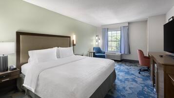 A hotel room with a large bed, a desk, a chair, a television, and a window with curtains.