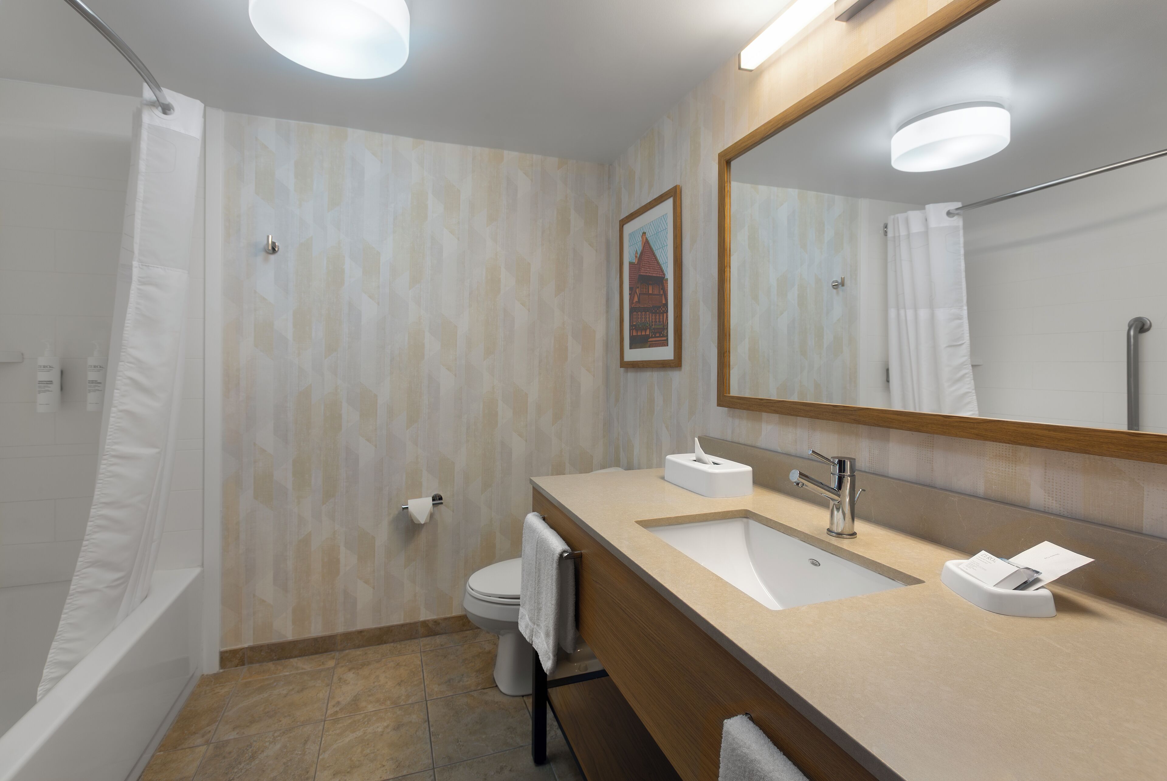 Uma casa de banho moderna com chuveiro, sanita, lavatório e um espelho grande.