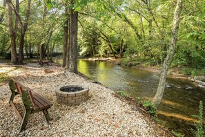 A bench and a fire pit in a wooded area with a river.