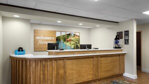 A reception desk with a 'Welcome to Hampton' sign, a 'Hulton Honors' plaque, and a 'Manager's Office' sign.