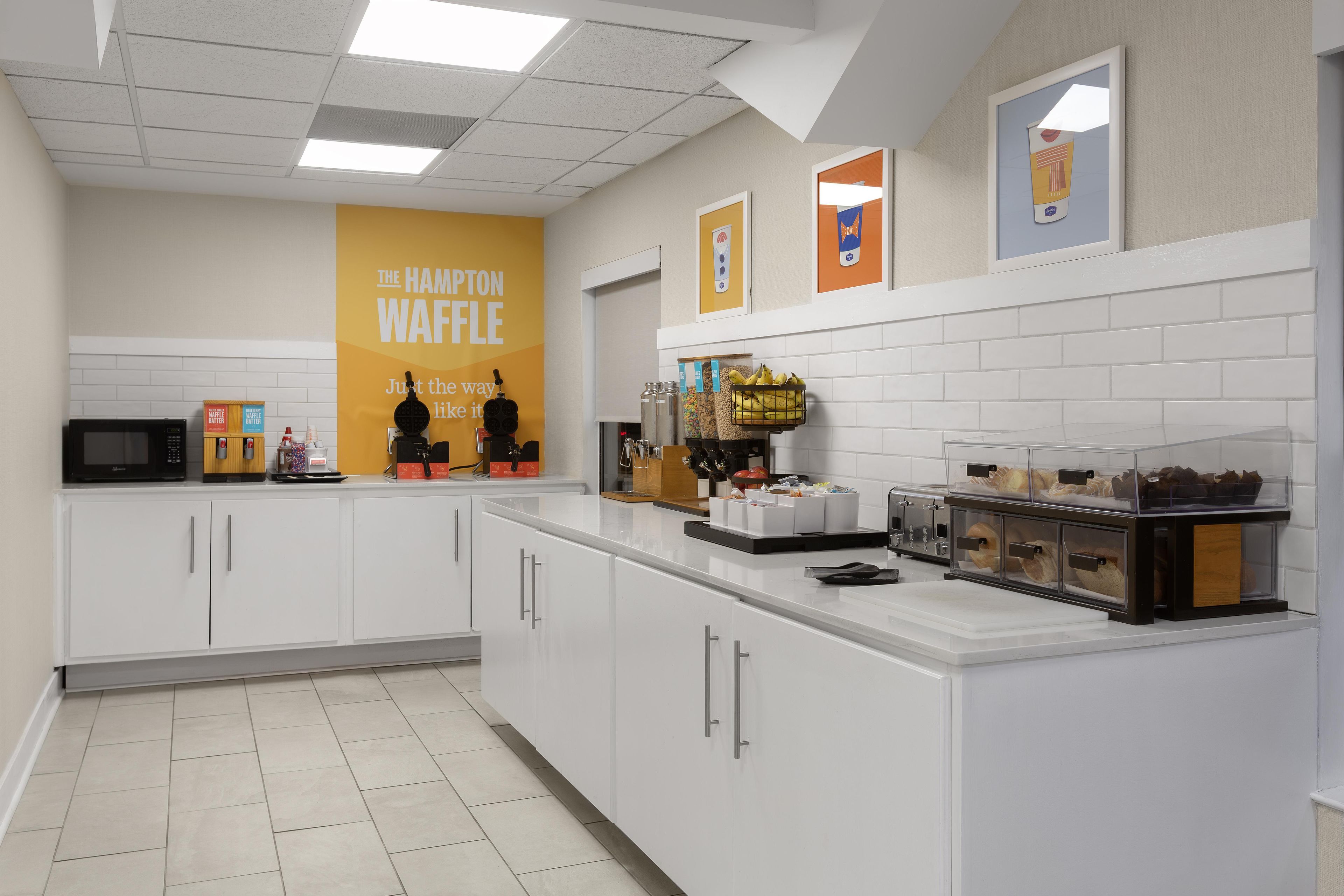 Una zona de cocina con una estación de waffles, microondas y diversos alimentos.
