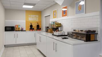 Una zona de cocina con una estación de waffles, microondas y diversos alimentos.