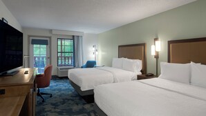 A hotel room with two beds, a desk with a TV, a chair, a window with a view, and a nightstand with a lamp. - Hampton Inn Helen (Helen)