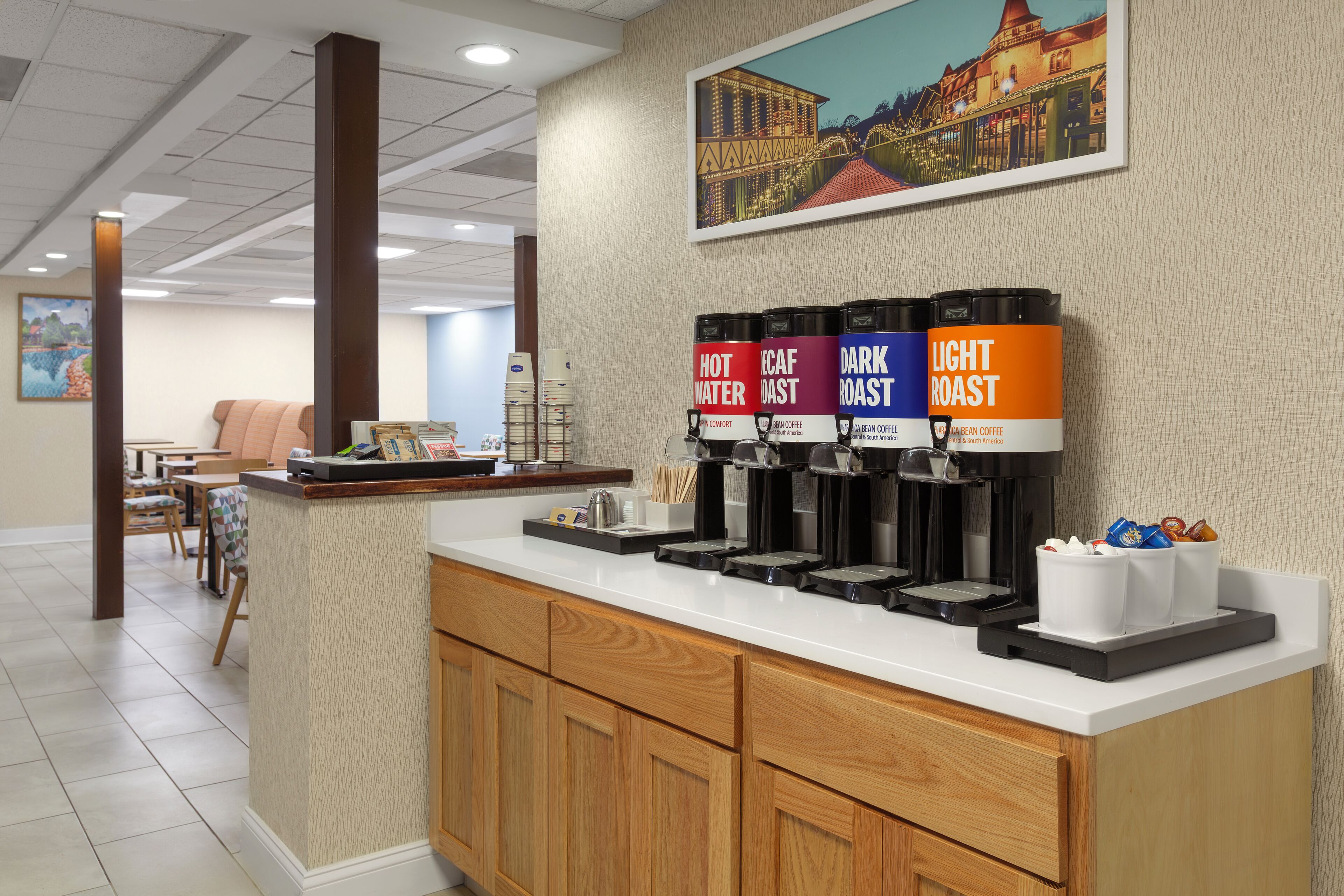 A coffee station with labeled dispensers for hot water, cream, dark roast, and light roast coffee.