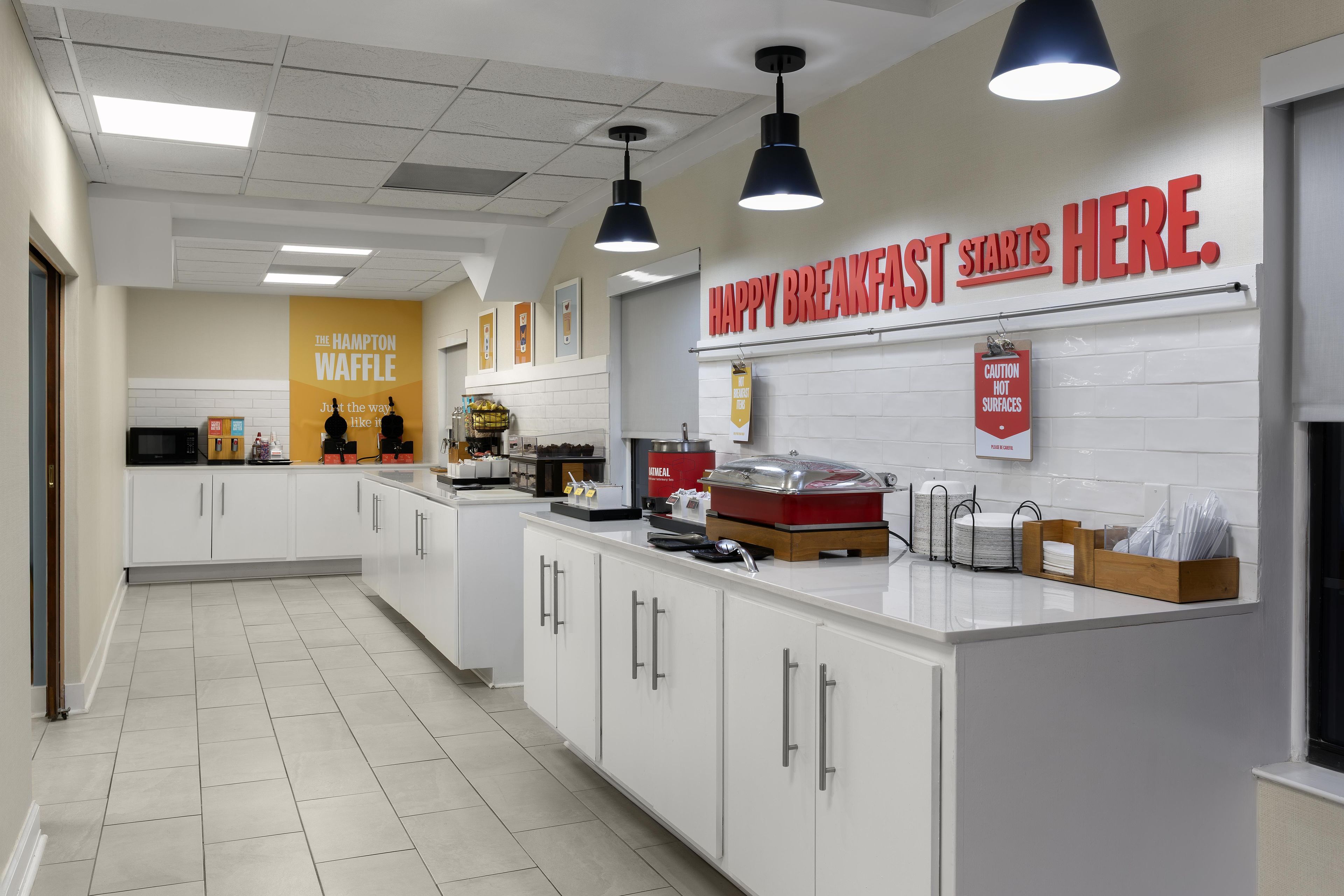 A modern kitchen with white cabinets, a breakfast bar, and a sign that reads 'HAPPY BREAKFAST STARTS HERE.'