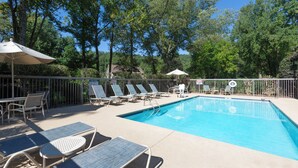 A swimming pool with lounge chairs and umbrellas, surrounded by trees and a fence.