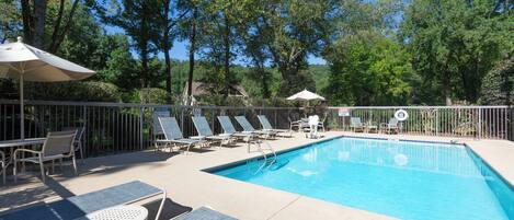 A swimming pool with lounge chairs and umbrellas, surrounded by trees and a fence.