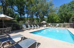 A swimming pool with lounge chairs and umbrellas, surrounded by trees and a fence.