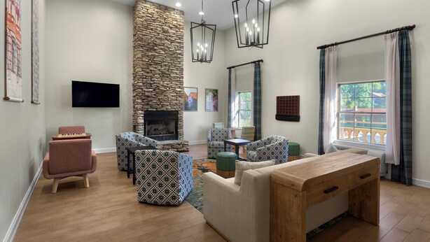 A living room with a stone fireplace, patterned furniture, a wooden coffee table, and a TV mounted on the wall. - Hampton Inn Helen (Helen)