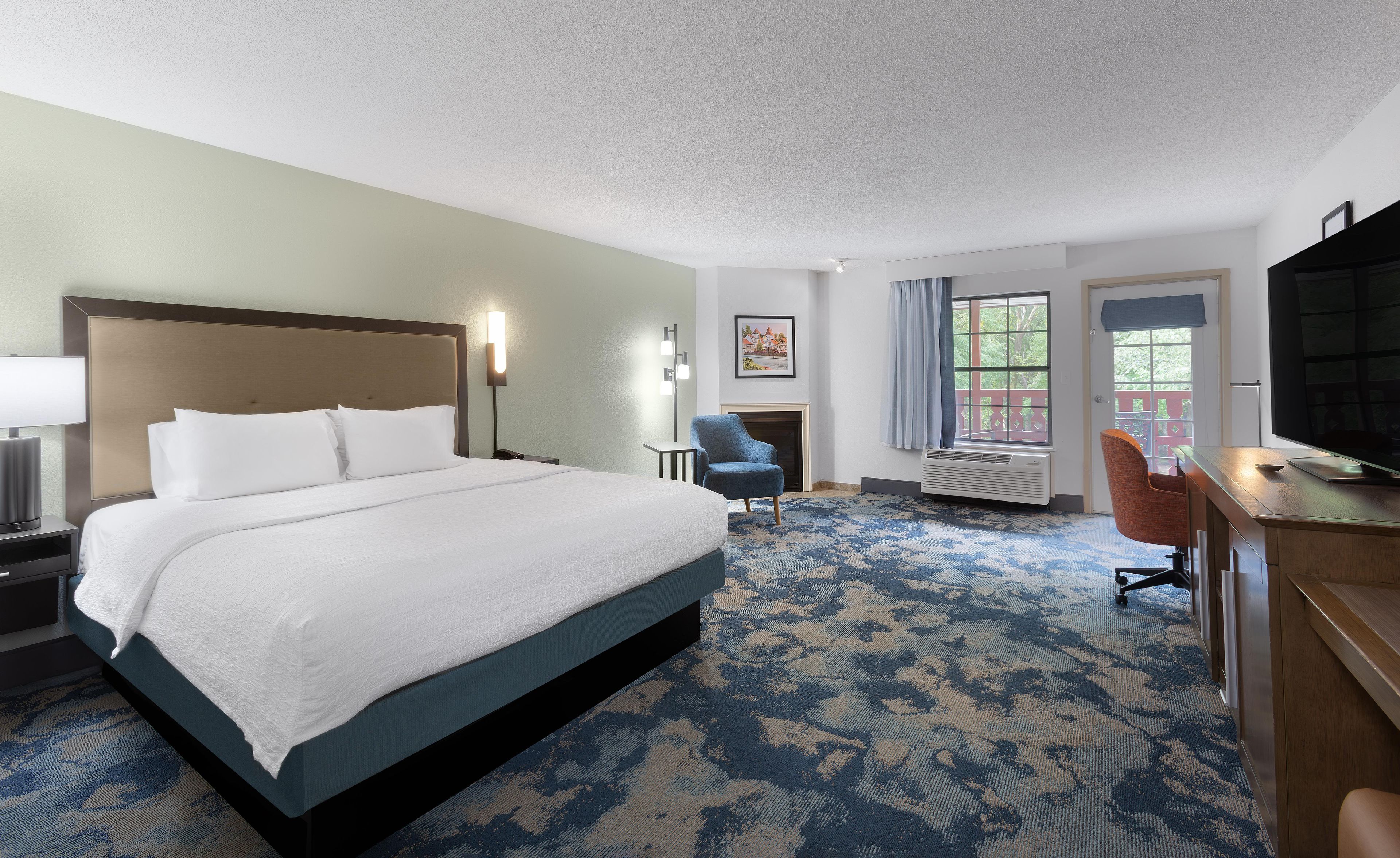 A hotel room with a large bed, a desk, a chair, a fireplace, and a television.