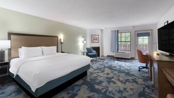 A hotel room with a large bed, a desk, a chair, a fireplace, and a television.