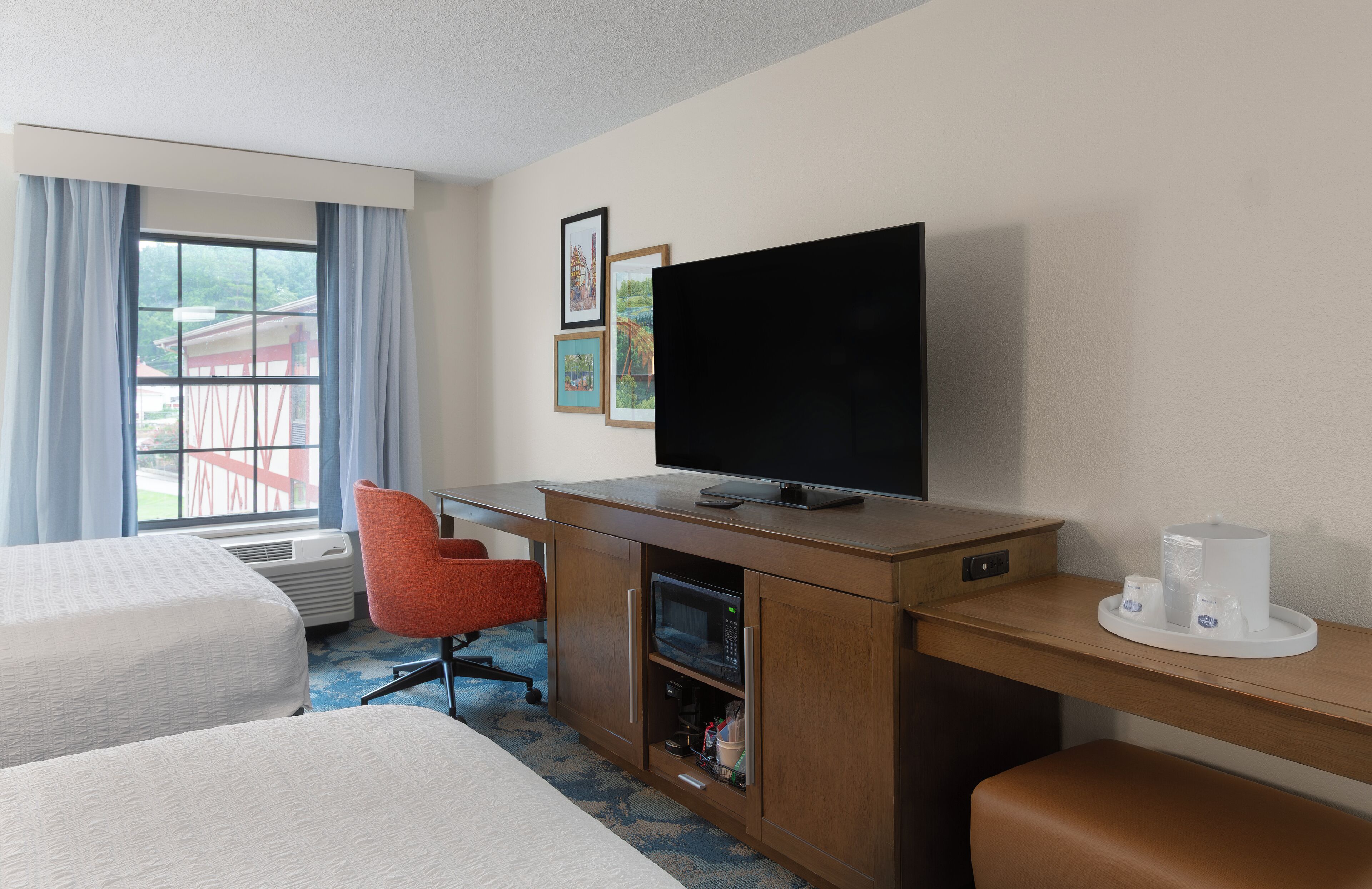 A hotel room with two beds, a desk with a flat-screen TV, a microwave, and a coffee maker.