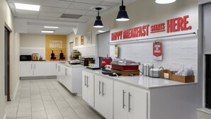 A modern kitchen with white cabinets, a central island, and overhead lighting. A sign on the wall reads "HAPPY BREAKFAST STARTS HERE." - Hampton Inn Helen (Helen)