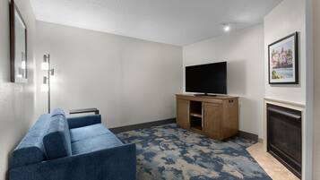 A modern living room with a blue sofa, a flat-screen TV on a wooden stand, a fireplace, and a patterned rug.