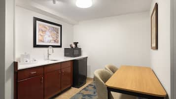 A compact kitchen with a microwave, coffee maker, and sink. There is a framed picture on the wall and a small table with chairs.