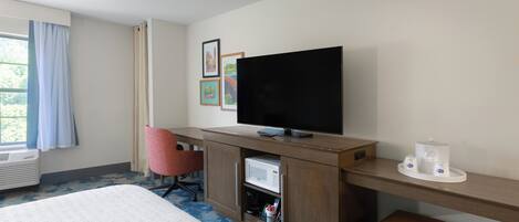 A hotel room with a bed, a desk with a television, a microwave, and a chair.