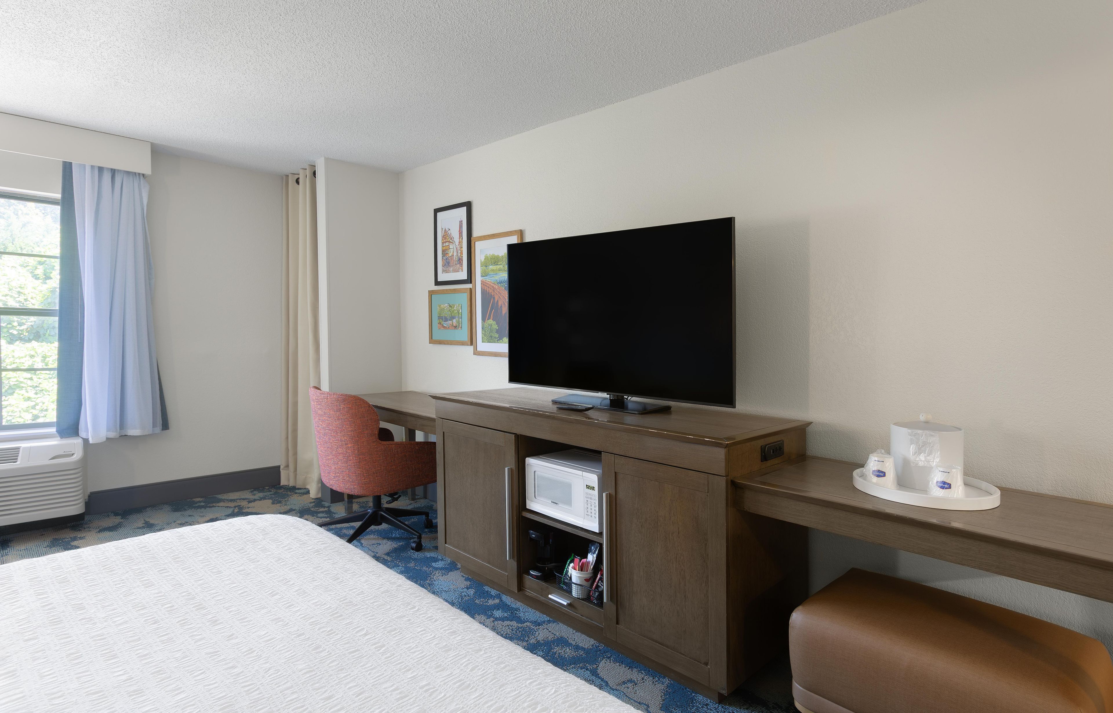 Habitación de hotel con cama, escritorio, televisión de pantalla plana, microondas y cafetera.