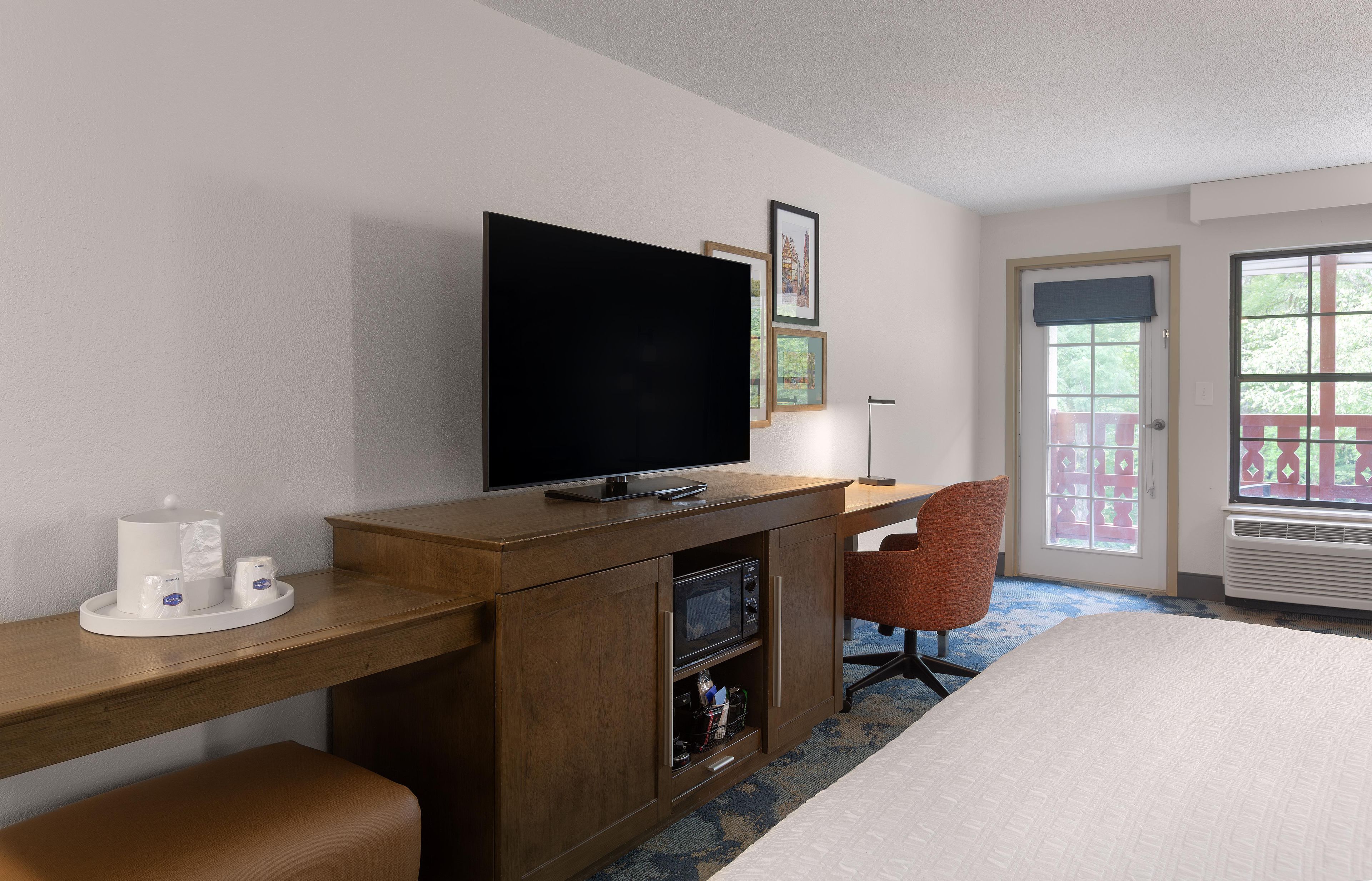 Une chambre d’hôtel avec un lit, un bureau avec une télévision, une chaise et une fenêtre donnant sur un paysage verdoyant.