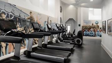 A gym with treadmills, stationary bikes, and a wall mural.