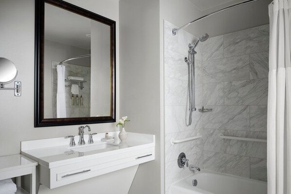 A modern bathroom with a white vanity, a large mirror, and a walk-in shower with a marble wall.
