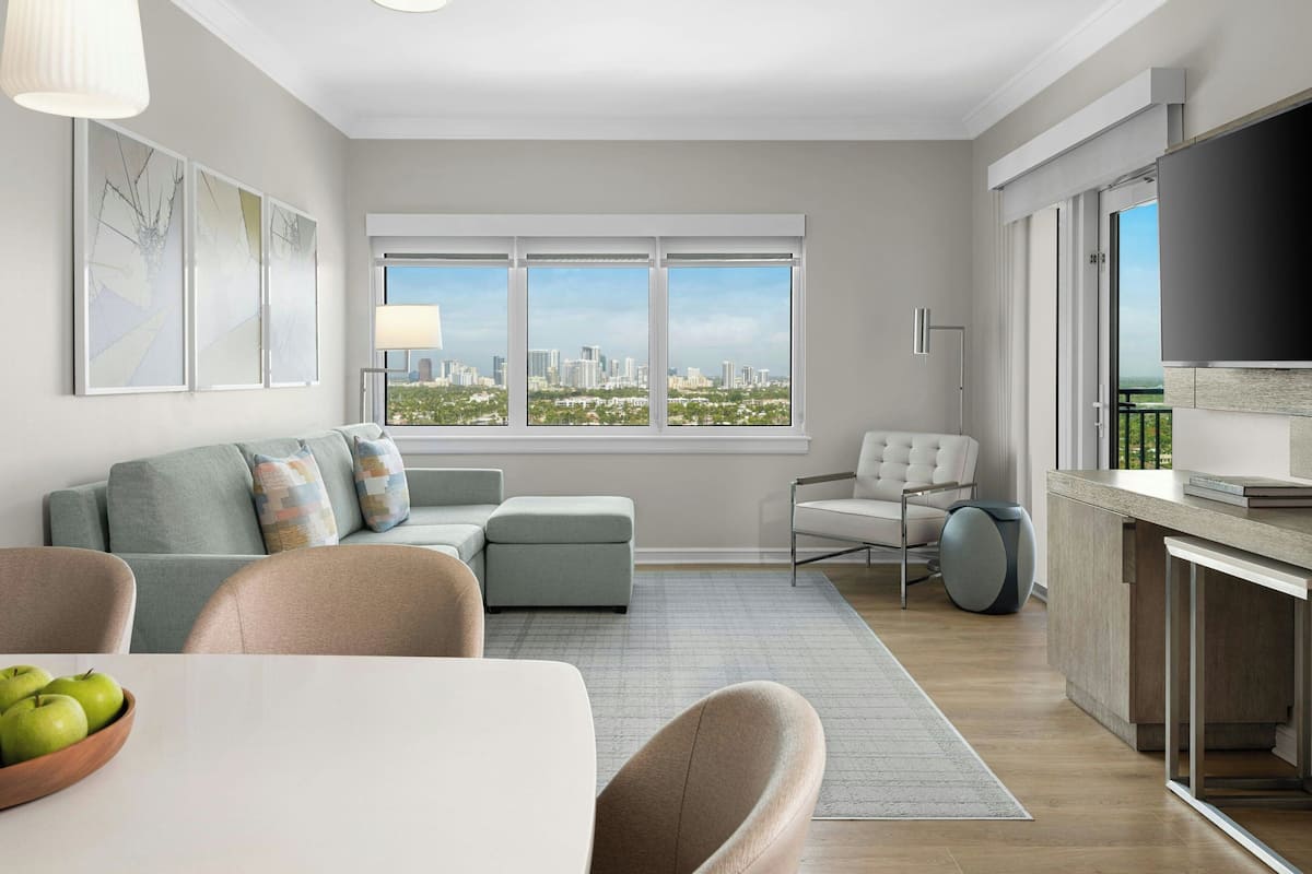 Een moderne woonkamer met een bank, fauteuil, eettafel en een groot raam met uitzicht over de stad.