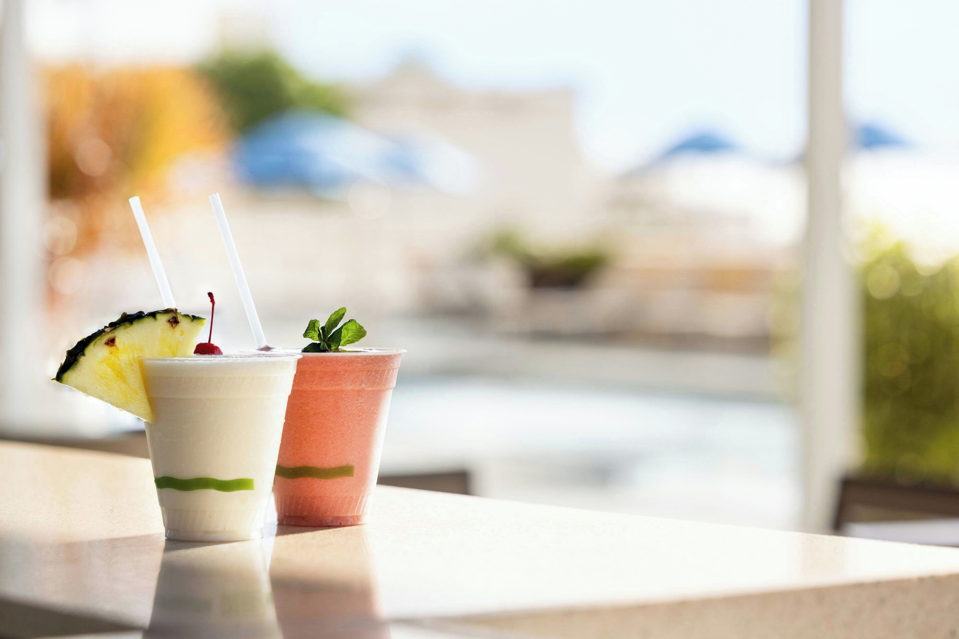 Deux boissons sur une table, avec une vue sur une plage et des parasols en arrière-plan.