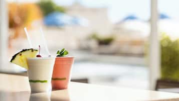 Deux boissons sur une table, avec une vue sur une plage et des parasols en arrière-plan.