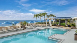 A pool area with lounge chairs, umbrellas, and a view of the ocean.