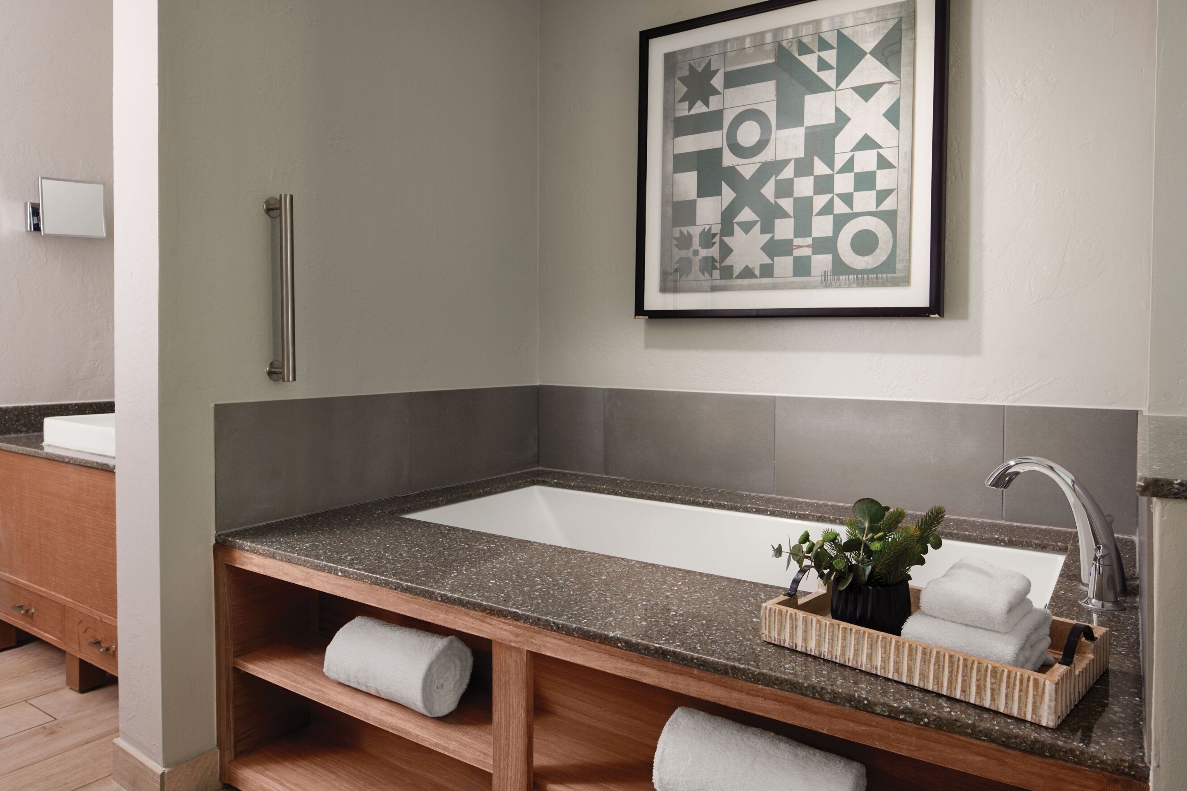 A bathroom with a rectangular sink, a towel rack, a framed abstract artwork, and a small plant on the countertop.