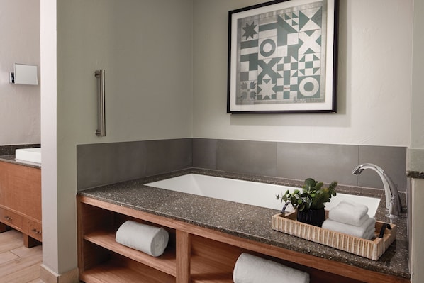Un baño con un lavamanos rectangular, un perchero, una obra de arte abstracta enmarcada y una planta pequeña en la encimera.