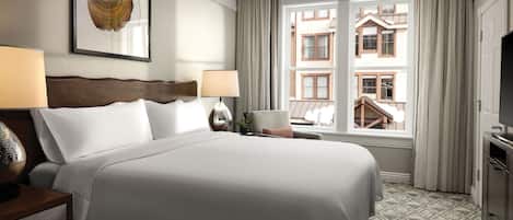 Habitación de hotel con una cama grande, dos lámparas de noche, una obra de arte enmarcada, vistas de edificios a través de la ventana y un televisor a la derecha.