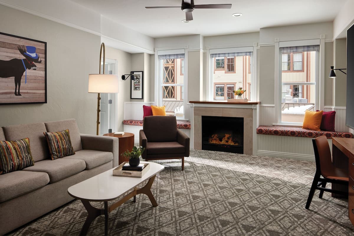 A living room with a sofa, armchair, coffee table, fireplace, and large windows with a view of the outside.